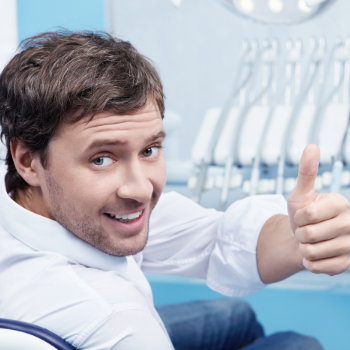 a man with a healthy smile shows his thumbs up in the dentist chair 1